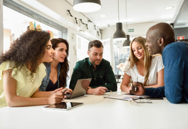 Five young people studying with laptop and tablet computers on white desk. Beautiful girls and guys working toghether wearing casual clothes. Multi-ethnic group smiling.